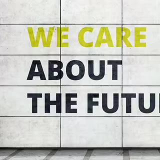 Eine helle Außenwand mit großen, rechteckigen Kacheln. Darauf steht in Großbuchstaben in hellem gelbgrün und dunklem blau in Englisch „we care about the future“. Übersetzung: „Wir kümmern uns um die Zukunft“.
